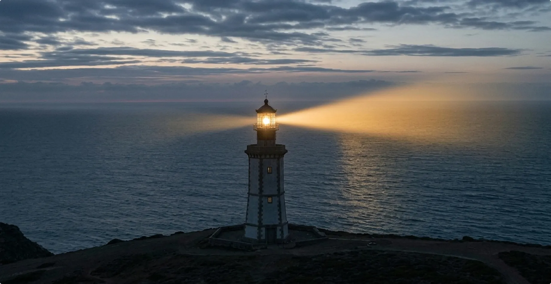 A lighthouse on a coastal cliff at twilight emitting a powerful beam of light, symbolising CorPower Ocean’s selection for the Mastercard Lighthouse MASSIV sustainability programme.
